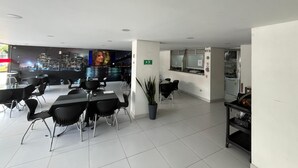 A modern dining area with a cityscape view, a large flat-screen TV, and a small bar area. - Hotel Portal Central (Itagüí)