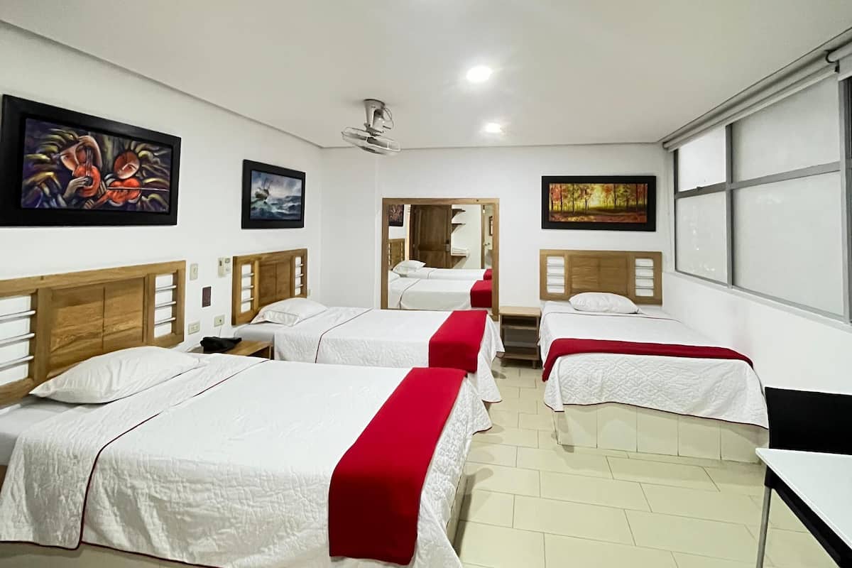 A hotel room with four beds, a ceiling fan, and artwork on the walls.