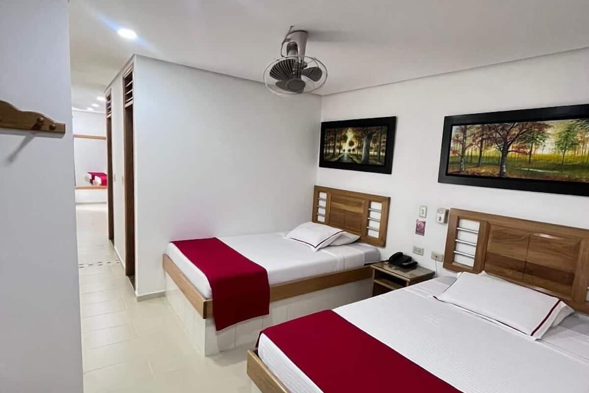 A hotel room with two beds, a ceiling fan, and artwork on the walls.
