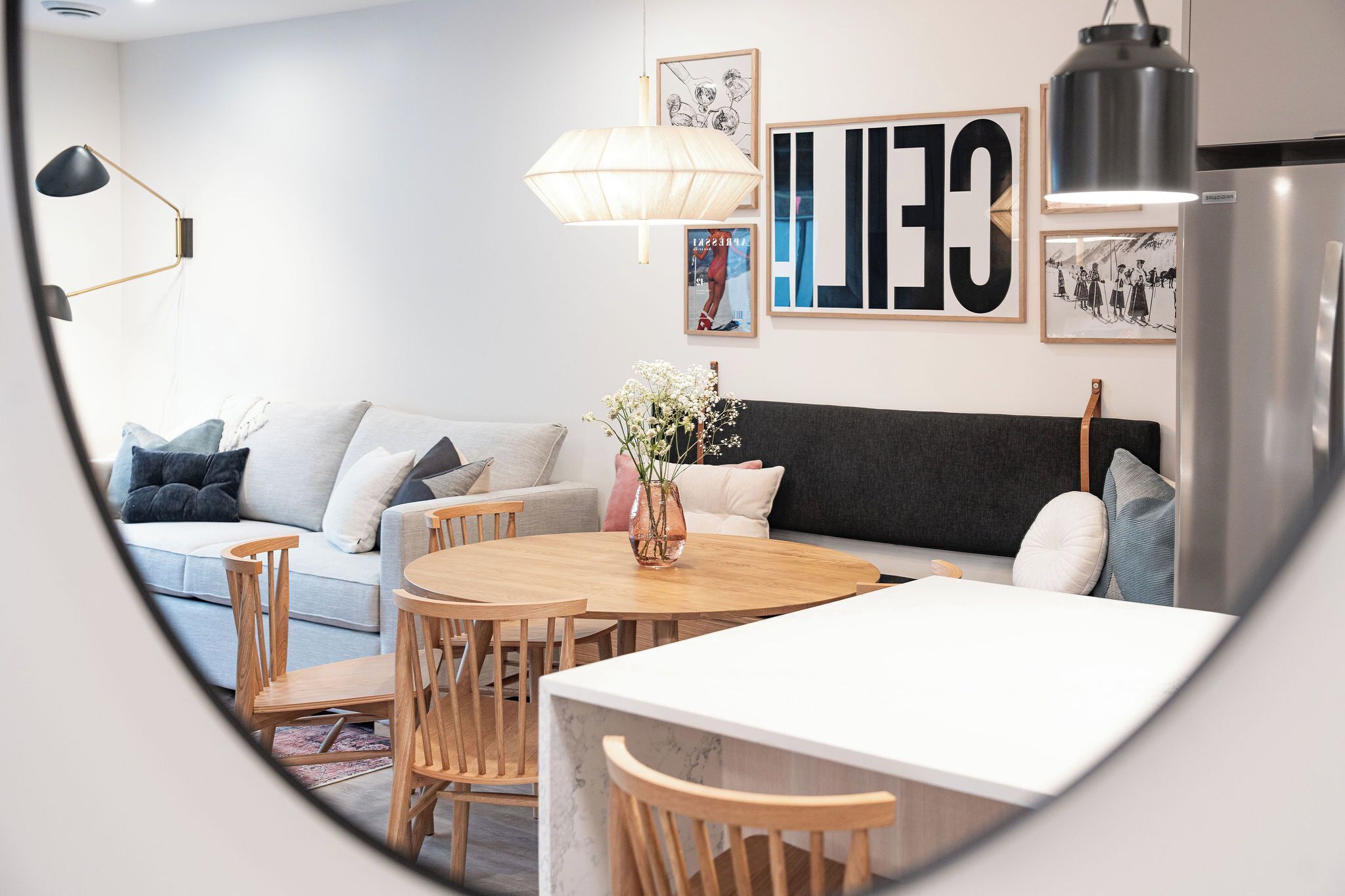 Ein modernes Wohnzimmer mit einer Couch, einem Esstisch und Stühlen. An der Wand hängt ein großes Kunstwerk und in der Ecke steht ein Kühlschrank.