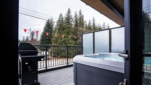 Ein Balkon mit Whirlpool, Grill und Blick auf Bäume sowie ein Fahrzeug im Hintergrund.