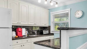 Una cocina con armarios blancos, una cafetera roja, un tostador y un reloj en la pared.