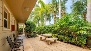 Un patio techado con mobiliario exterior, rodeado de abundante vegetación y palmeras.