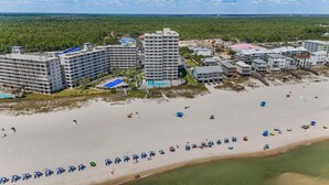 Un complexe hôtelier situé sur la côte, composé de plusieurs immeubles de grande hauteur, d’une plage de sable et de nombreux parasols.