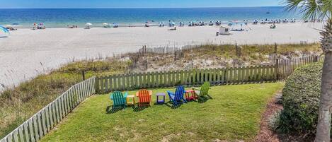 A beach view with a grassy area and colorful Adirondack chairs.