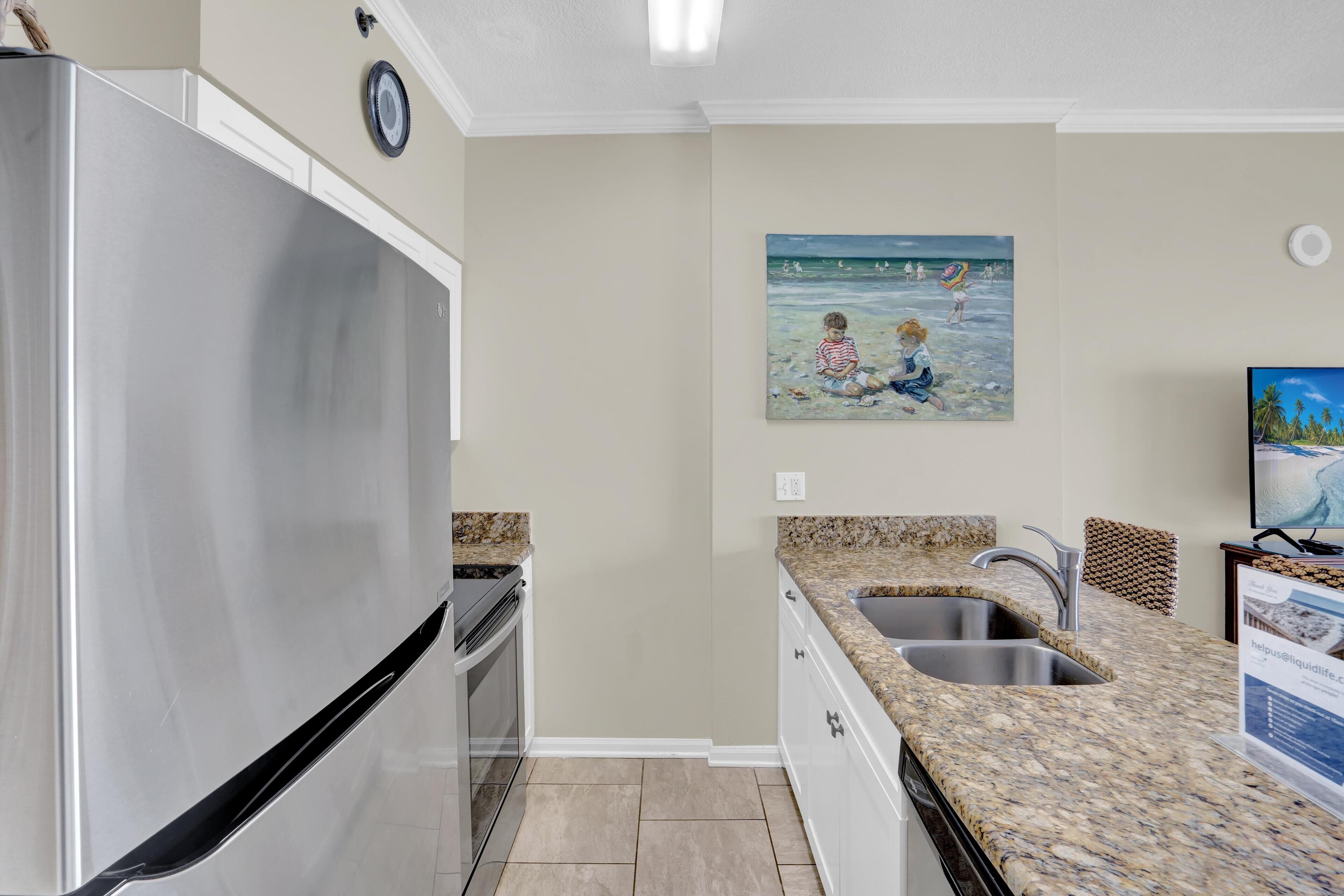 A kitchen with a stainless steel refrigerator, granite countertops, a double sink, and a painting of children at the beach.