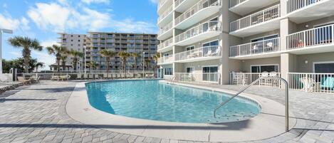 A swimming pool with a curved edge, surrounded by a paved walkway.
