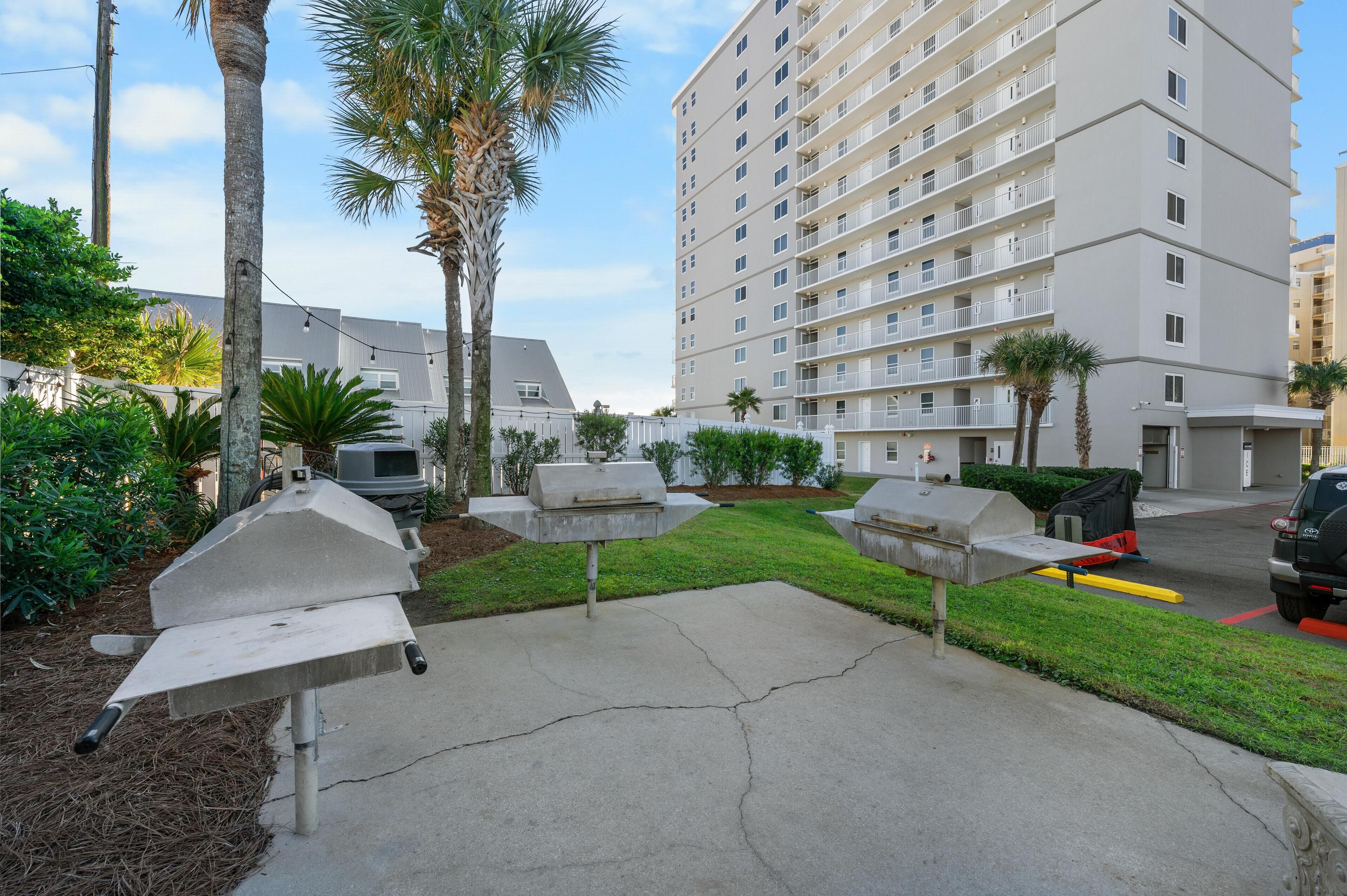 A residential area with a multi-story building, outdoor grills, and palm trees.