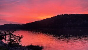 Ein Sonnenuntergang über einem stillen See mit einem bewaldeten Hang im Hintergrund.