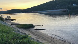 Aussicht auf einen Fluss mit angestoßenen Booten, einem Sandstrand und einer bewaldeten Hügelkette im Hintergrund.