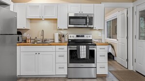 Una cocina moderna con armarios blancos, un refrigerador de acero inoxidable, un microondas y una estufa.