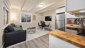 Una cocina compacta con refrigerador integrado, un comedor con mesa y sillas, y una sala de estar con sofá y lámpara.