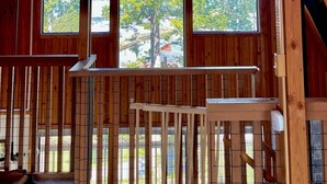 A wooden cabin with a sloped ceiling, a ceiling fan, and three large windows offering a view of trees and a building outside. - Charming Pet-Friendly Cabin with Sunset Views Over Birch Bay (Blaine)