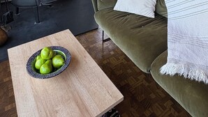 A cozy living room with a stone wall, a fireplace, a sofa, a table with a bowl of fruit, and a staircase. - Charming Pet-Friendly Cabin with Sunset Views Over Birch Bay (Blaine)