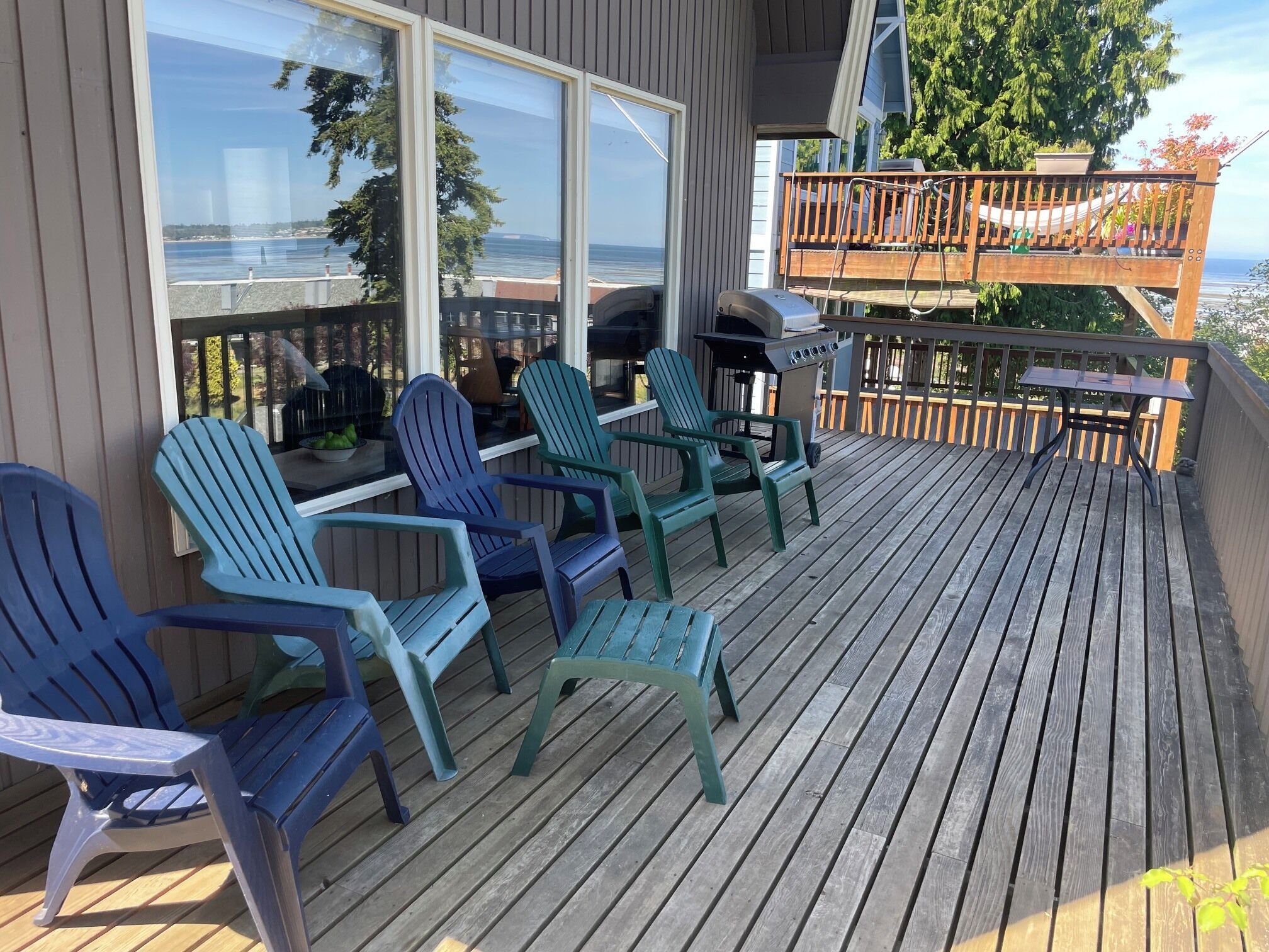 A deck with Adirondack chairs, a grill, and a view of the ocean.