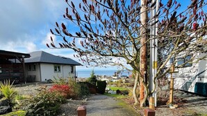 A pathway leading to a building with a view of the sea, surrounded by gravel and plants. - Charming Pet-Friendly Cabin with Sunset Views Over Birch Bay (Blaine)