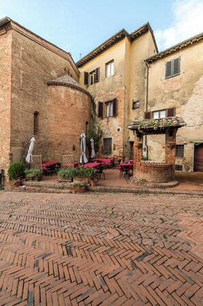 A courtyard with brick flooring, outdoor tables with umbrellas, and a brick fountain. - Borgo Antico Residence  (Certaldo)