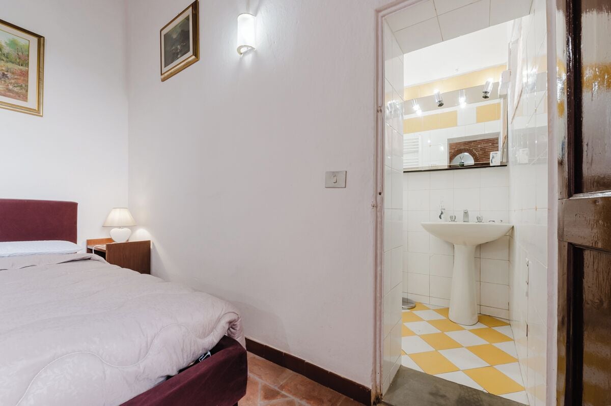 Une chambre à coucher avec un lit, une lampe de chevet et une vue sur une salle de bain équipée d’un lavabo et dont le sol est carrelé.
