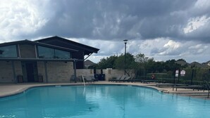 A swimming pool with a clear blue water surface, surrounded by a stone deck and a building with a modern design. - Spacious 3-bedroom house with AC, fitness room, WiFi in Leander/North Austin (Leander)