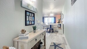 A hallway with a welcome sign, a framed welcome sign, a small table with candles, and a starfish rug.