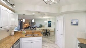 A modern kitchen with white cabinets, granite countertops, and a central island with a sink. There is a dining area with a table and chairs in the background.