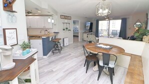 A modern kitchen with white cabinets, a central island, and a dining area with a wooden table and chairs.