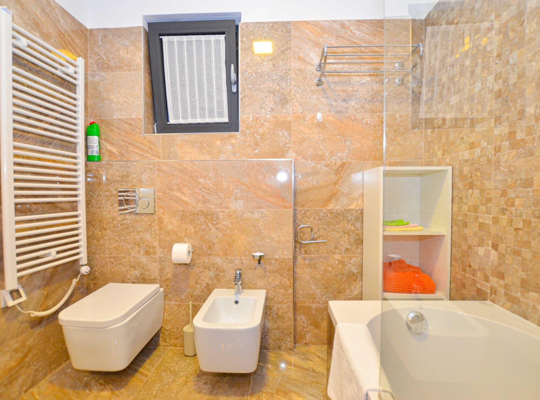 A bathroom with a bidet, a toilet, a bathtub, a towel rack, and a shower area.