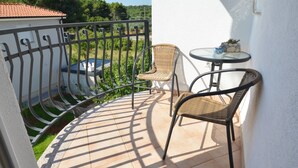 Ein Balkon mit Fliesenboden, zwei Korbstühlen, einem kleinen runden Tisch und einem Metallgeländer.