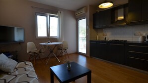 Ein modernes Wohnzimmer mit einer Couch, einem kleinen runden Tisch und einem Fernseher. Es gibt eine Küchenzeile mit dunklen Schränken und einem Herd.