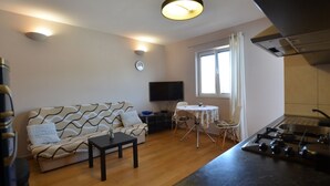 Ein kompakter Wohnraum mit Sofa, Esstisch, Fernseher und einer Küchenzeile mit Herd.
