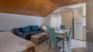Une pièce de taille modeste avec un plafond en bois, un canapé, une table à manger avec des chaises, un petit coin cuisine équipé d’un réfrigérateur et une fenêtre avec des rideaux.