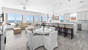 A spacious living room with a large sofa, a round dining table, and a kitchen area with a view of the ocean. - 5-Bed Beach House with Private Pool (Panama City Beach)