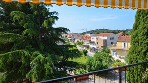 Ein Balkon mit gestreiftem Jalousiewindfang, der auf ein Wohngebiet mit Häusern und Grünflächen blickt.