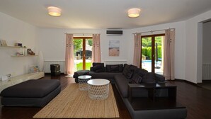 A modern living room with a sectional sofa, a round coffee table, and a TV. There are two windows with curtains, a radiator, and a bookshelf. - Sophisticated and Chic Villa with Pool - Four Bedroom Villa with Pool (Kanfanar)