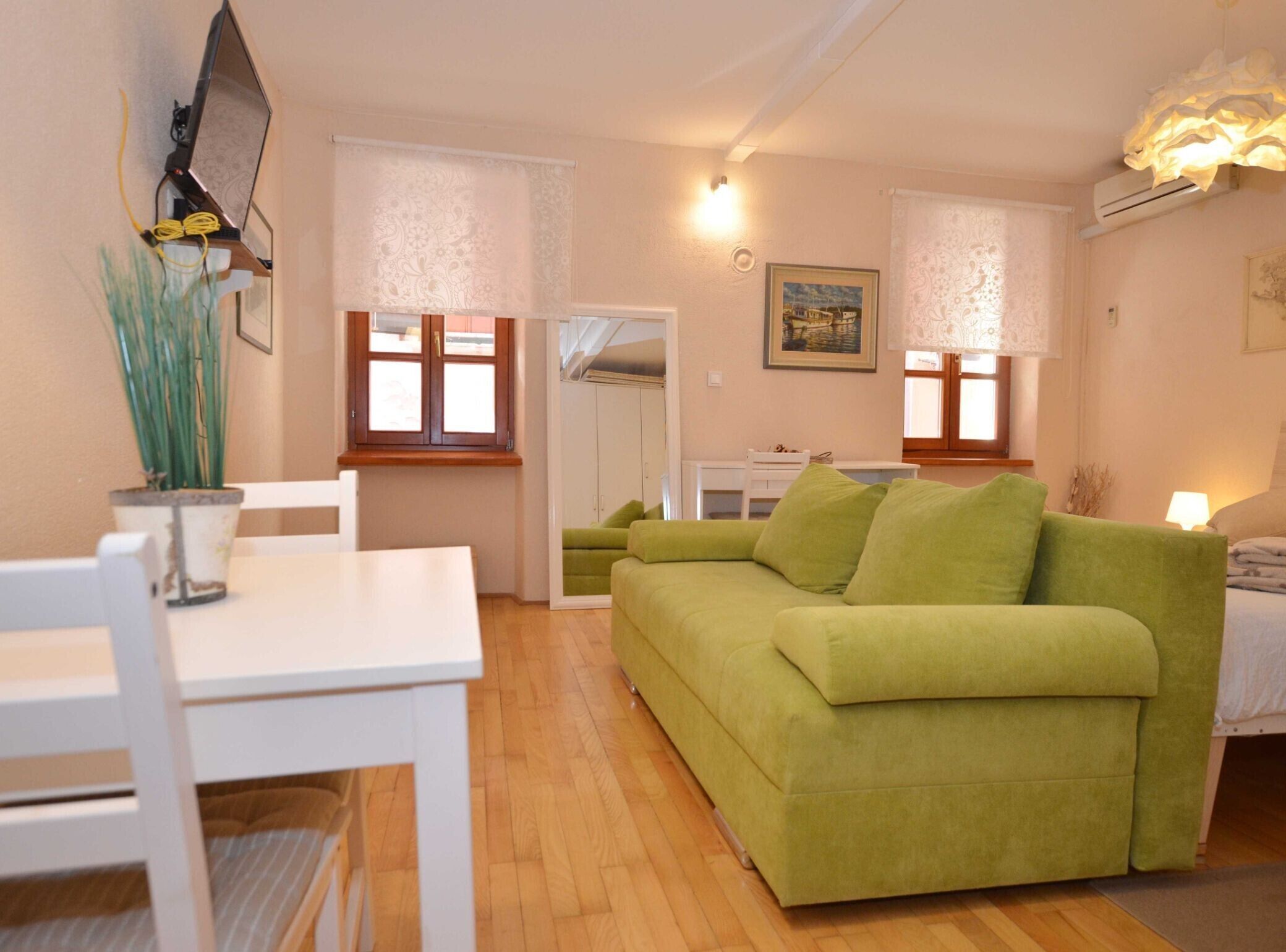 Ein gemütliches Wohnzimmer mit einem grünen Sofa, einem weißen Esstisch und einer kleinen, weißen Kommode.