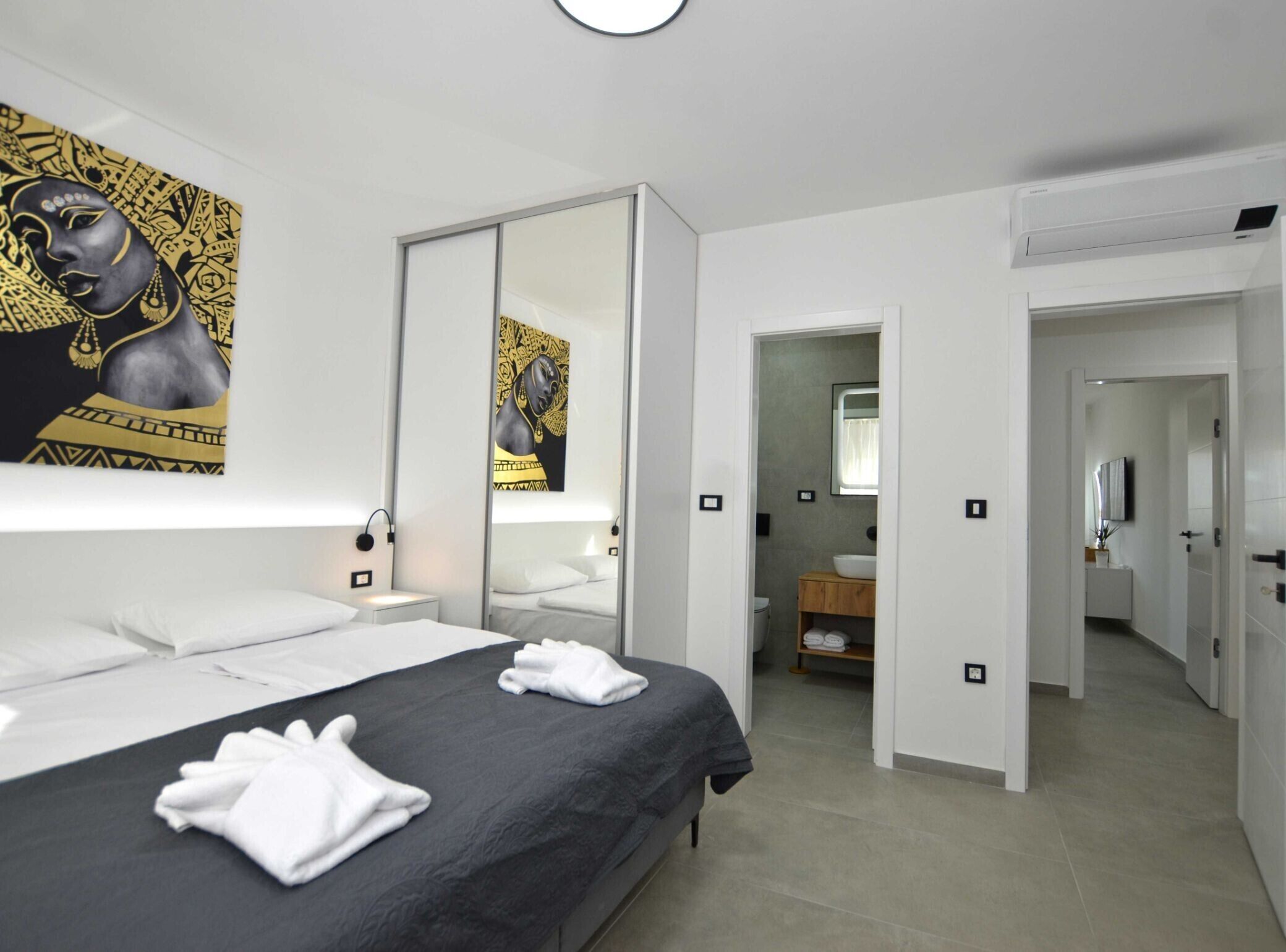 A modern hotel room with a large bed, a bedside table, a mirror, and artwork on the wall.