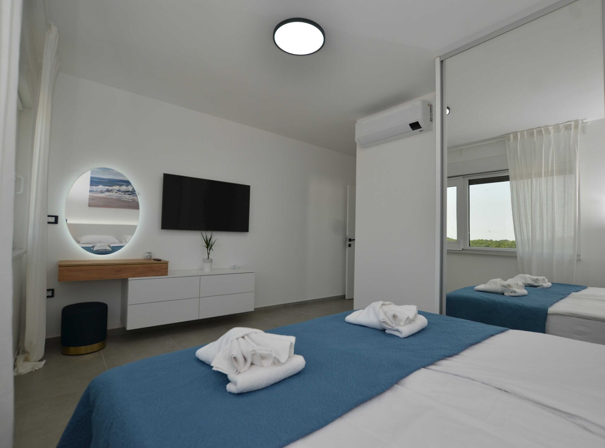 Ein Hotelzimmer mit Bett, Nachttisch, Spiegel, Fernseher und einem Fenster mit Vorhängen.