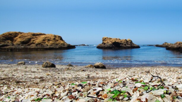 Une plage de galets parsemée de rochers, avec une eau d’un bleu limpide.