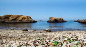 Una playa de guijarros con rocas dispersas y agua azul cristalina.
