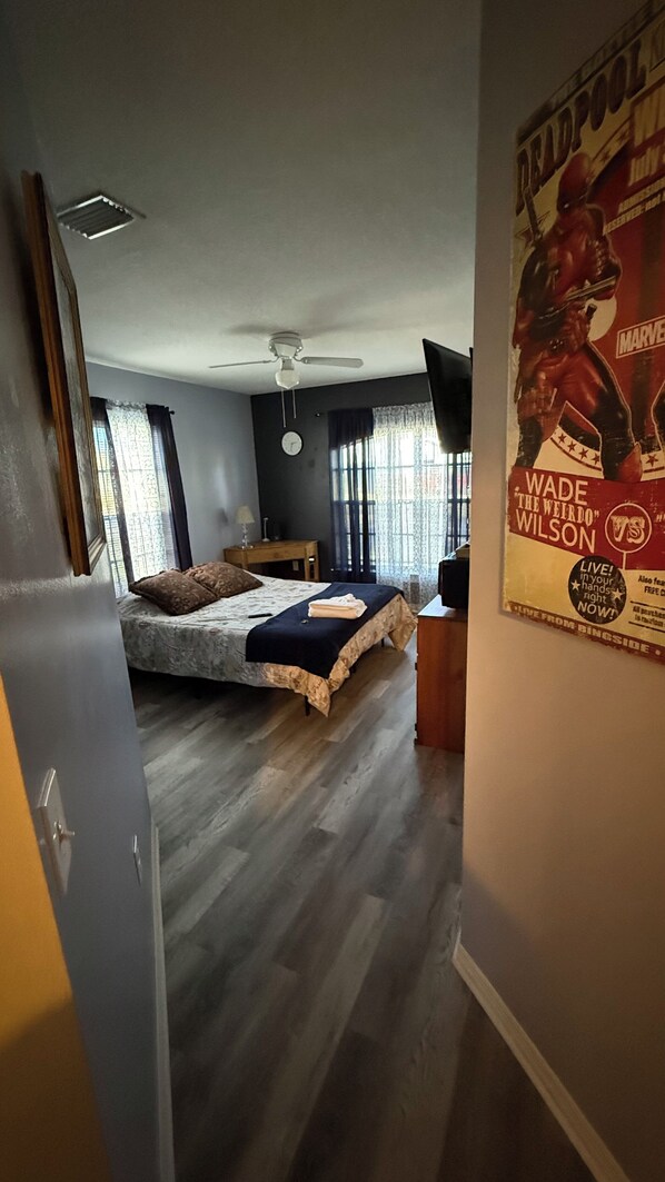A bedroom with a bed, a ceiling fan, a window, and a poster on the wall. - Charming Latin family room for 1 Guest (Palm Bay)