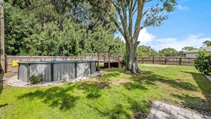 A backyard with a wooden deck, a large tree, and a swimming pool.
