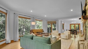 A spacious living room with a green sofa, leather armchair, and a dining area with a table and chairs. - Big Sam's Riverside Retreat (Stanfield)