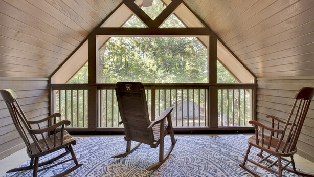 A wooden interior with a sloped ceiling and a view of trees through a large window. There are two rocking chairs and a patterned floor. - Big Sam's Riverside Retreat (Stanfield)