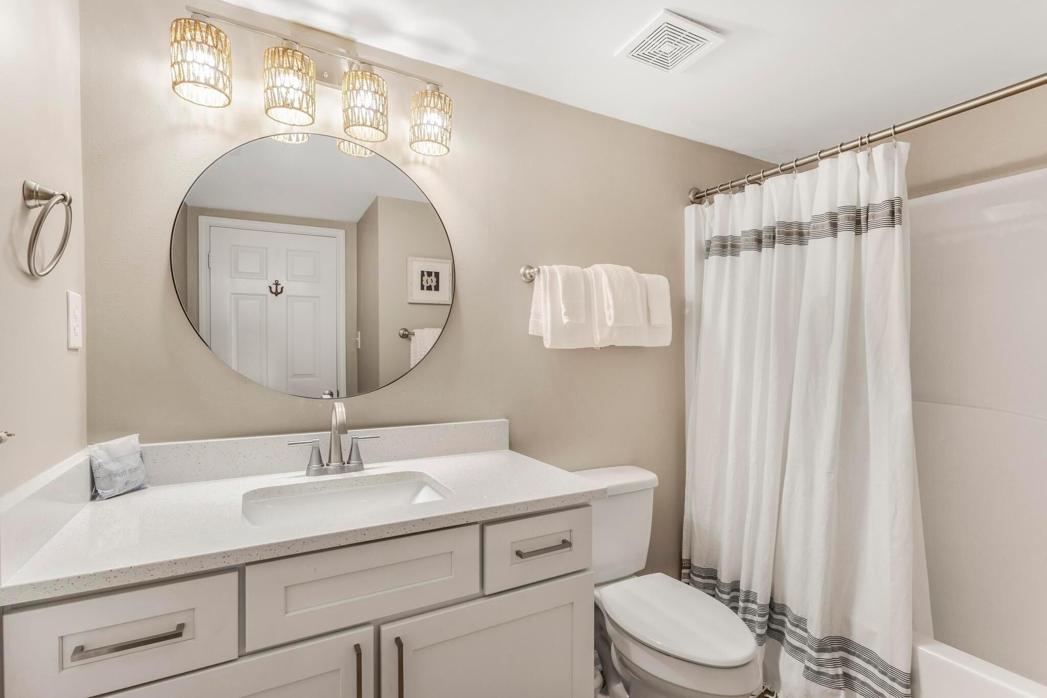 A bathroom with a round mirror, white sink, and toilet. There are three wall-mounted lights above the mirror and a shower curtain with a striped pattern.