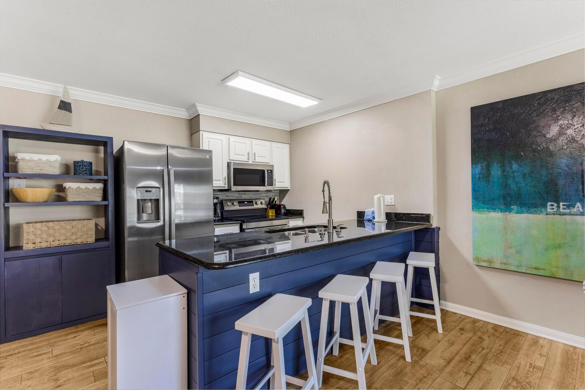 A modern kitchen with a central island, bar stools, and a microwave.