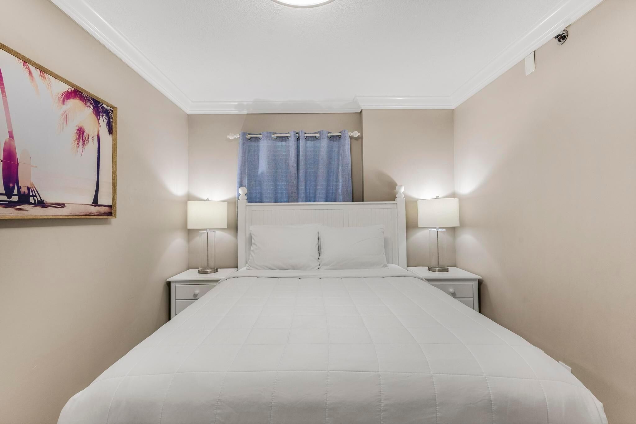 A hotel room with a bed, two bedside tables, a nightstand, a window with curtains, and a wall-mounted painting.