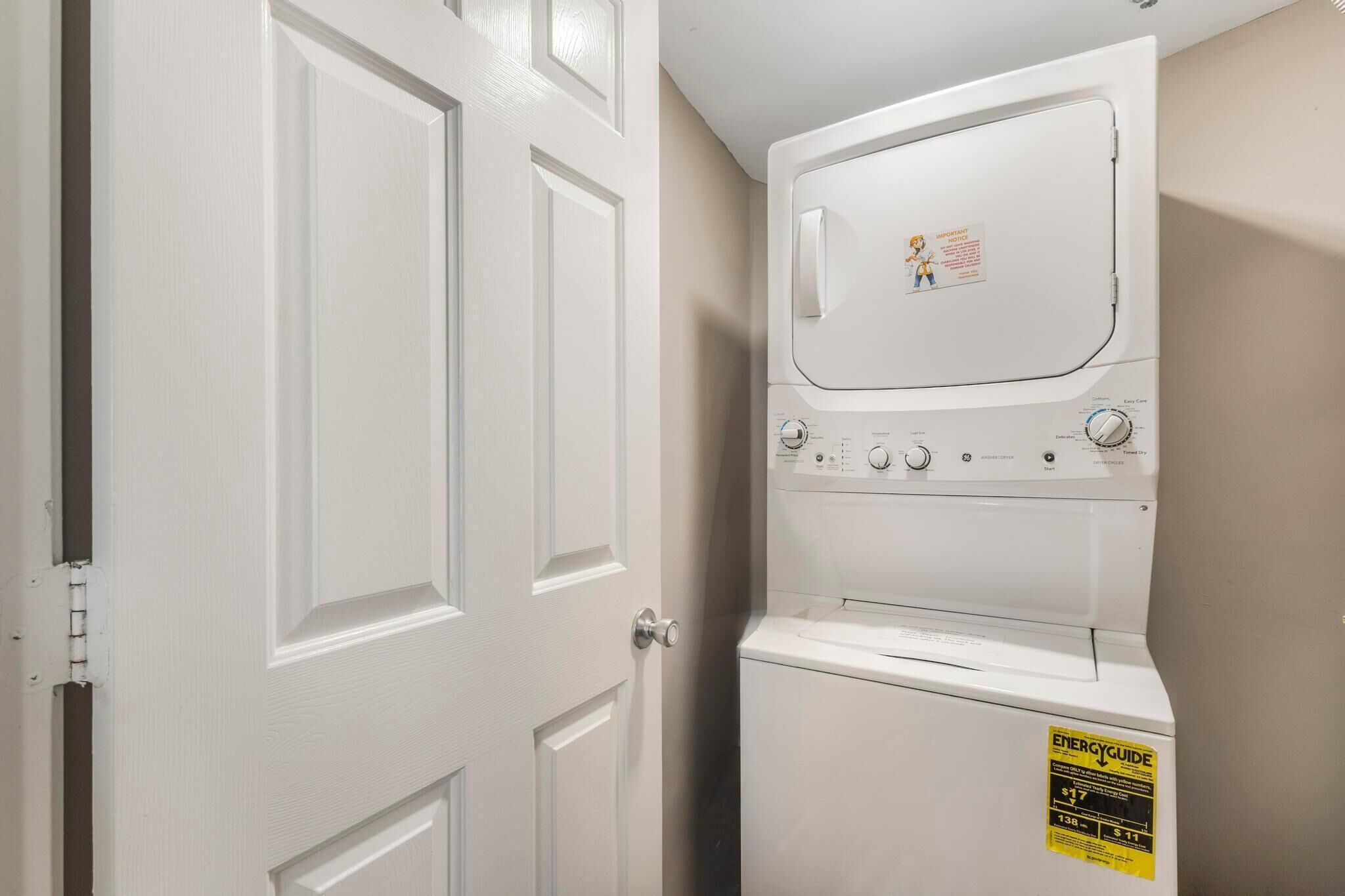 A laundry room with a stacked washer and dryer, a door with a lock, and an ENERGY GUIDE sticker on the dryer.