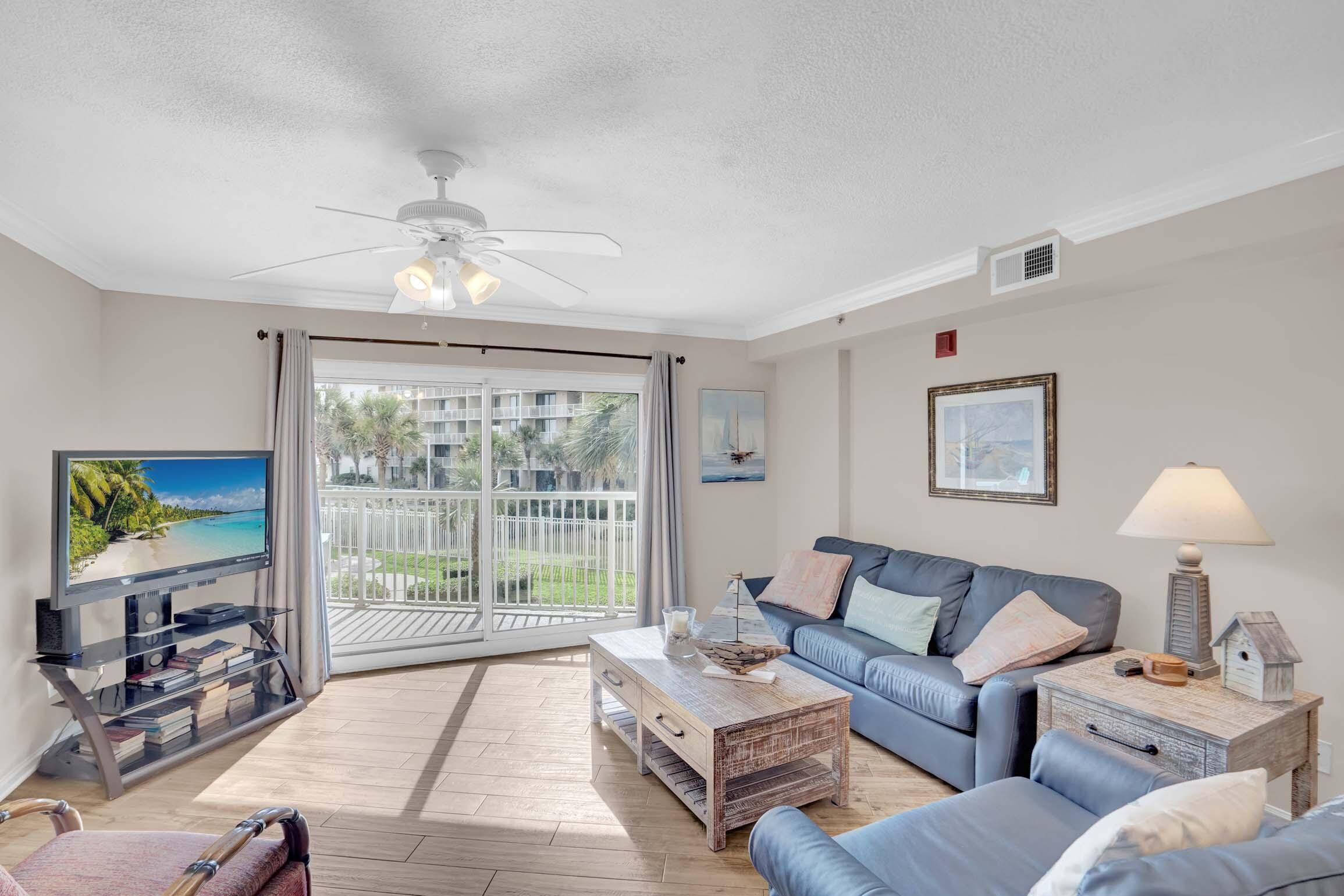 A living room with a TV, blue sofas, a coffee table, and a ceiling fan.