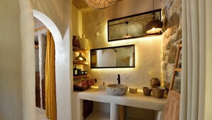 A bathroom with a stone wall, a large mirror, a sink with a stone basin, and a wooden bench. - Chi House (Ayvalik)
