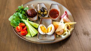 A plate with various foods including sliced cucumbers, tomatoes, boiled eggs, cheese, olives, and meat. - Chi House (Ayvalik)